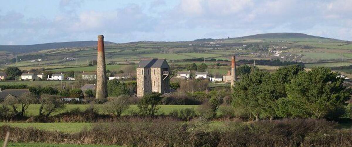 A rural landscape with a stone tower, two chimneys, and a small building.