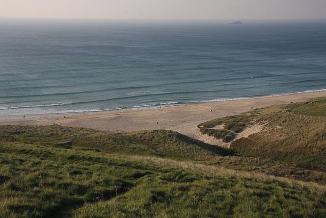 A coastal landscape with a sandy beach, grassy dunes, and the ocean.