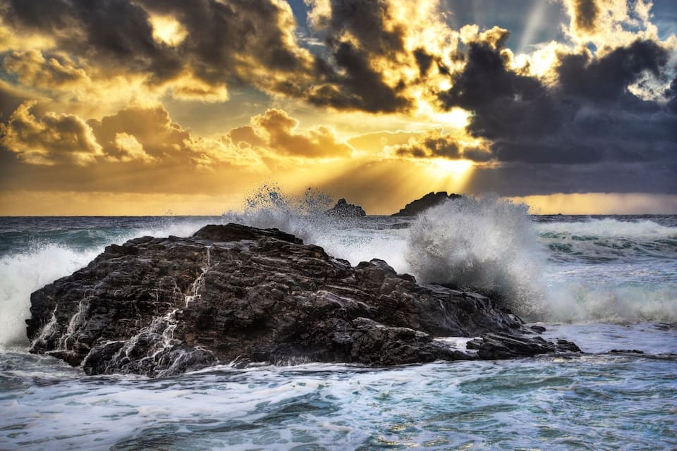 A rocky coastline with waves crashing against the rocks under a dramatic sunset sky.