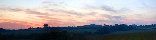 A sunset over a rural landscape with fields and distant trees.
