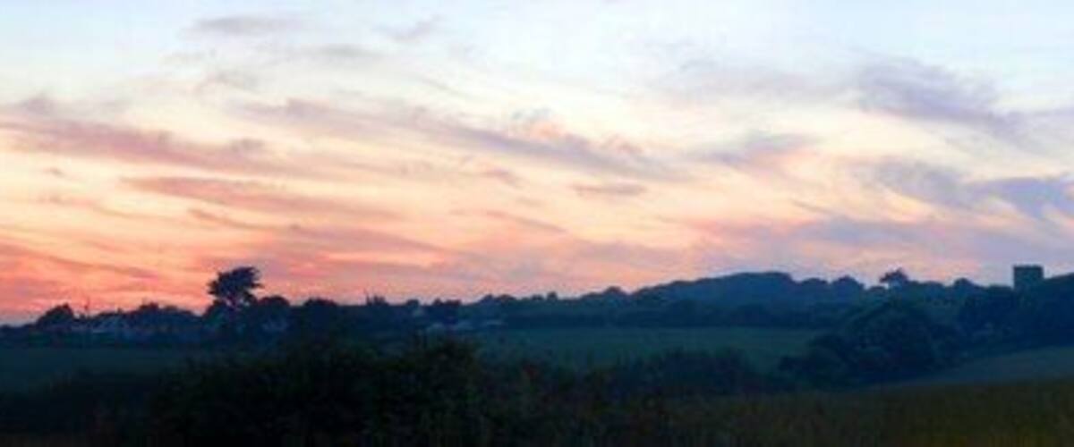 A sunset over a rural landscape with fields and distant trees.