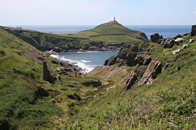 A coastal landscape with a hilltop lighthouse, rocky cliffs, and a body of water.