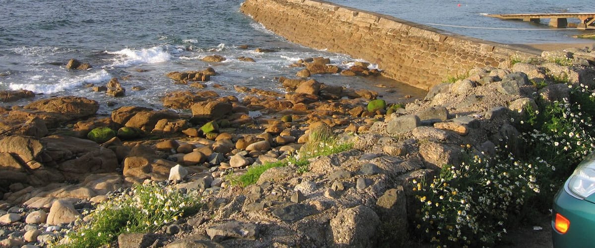 A rocky coastline with a stone sea wall and a small pier.
