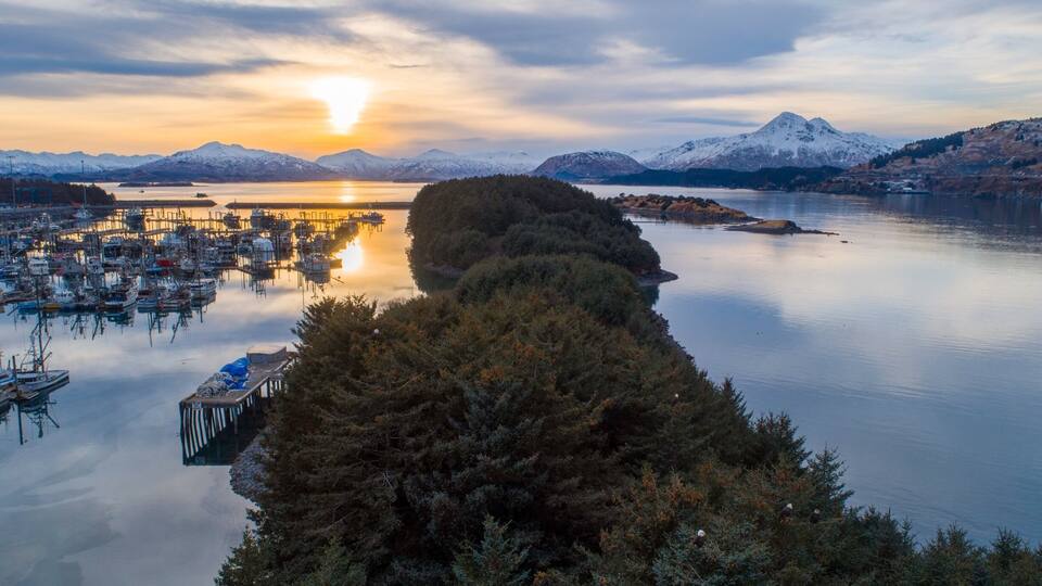A serene harbor with boats, a dock, and a backdrop of snow-capped mountains at sunset.