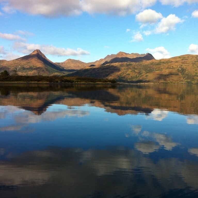 A mountain range reflected in a calm lake with clear skies.