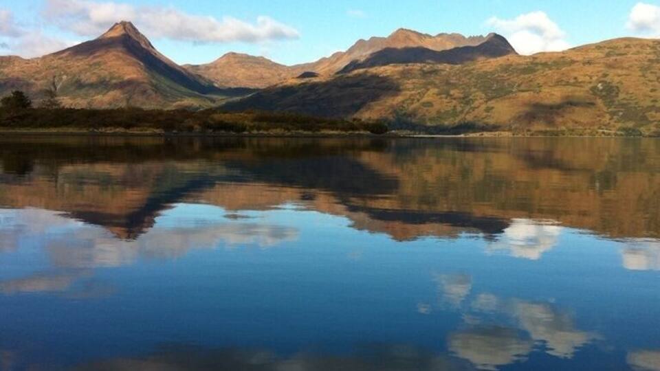 A mountain range reflected in a calm lake with clear skies.