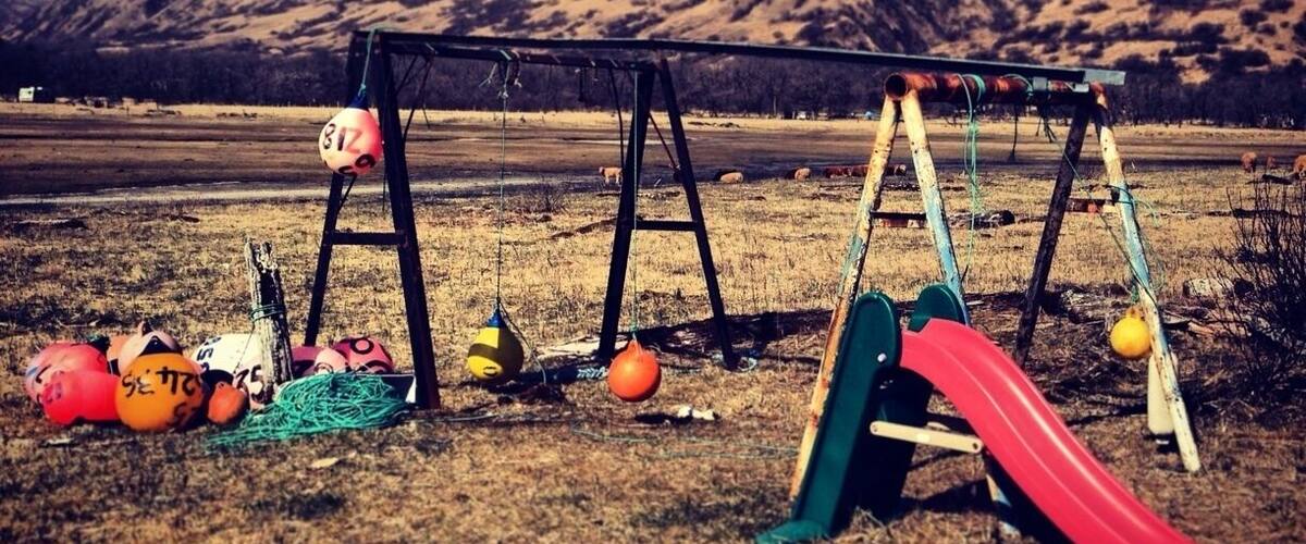 A playground with swings and a slide, surrounded by a grassy field and mountains in the background.