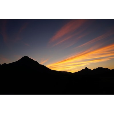 A mountain range silhouetted against a sunset sky with vibrant orange and yellow hues.