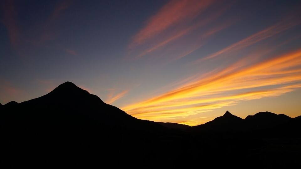 A mountain range silhouetted against a sunset sky with vibrant orange and yellow hues.