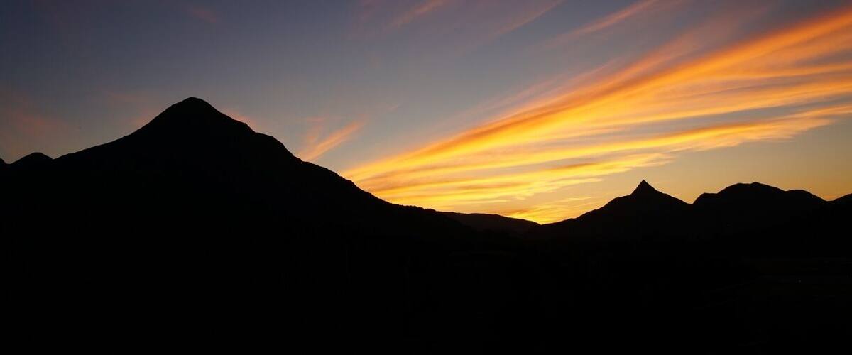 A mountain range silhouetted against a sunset sky with vibrant orange and yellow hues.