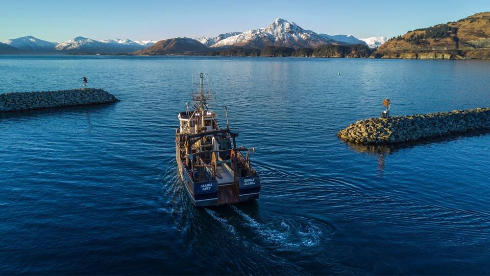 A boat named 'KODIKK DAWN' on a lake with mountains in the background.