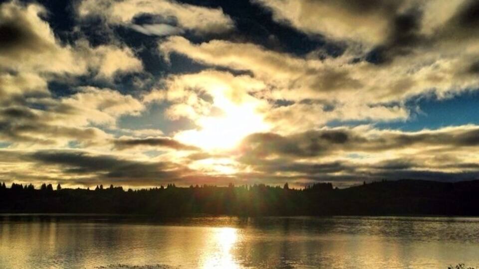 A sunset over a calm lake with a silhouette of trees in the background.