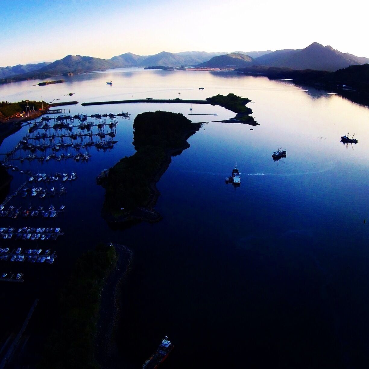 A marina with boats docked, a calm lake, and mountains in the background.