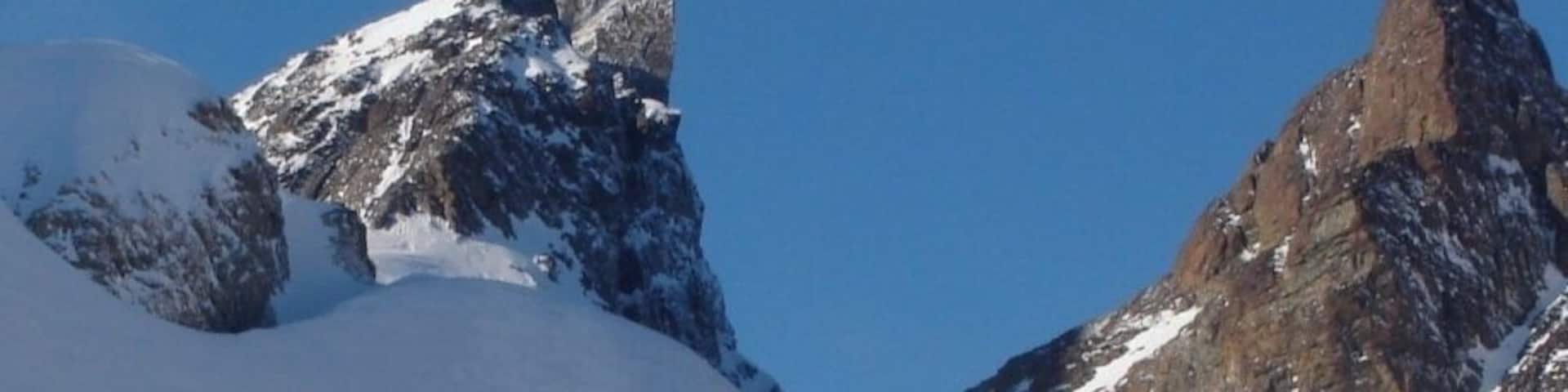 A snowy mountain landscape with ski tracks and a rocky peak.