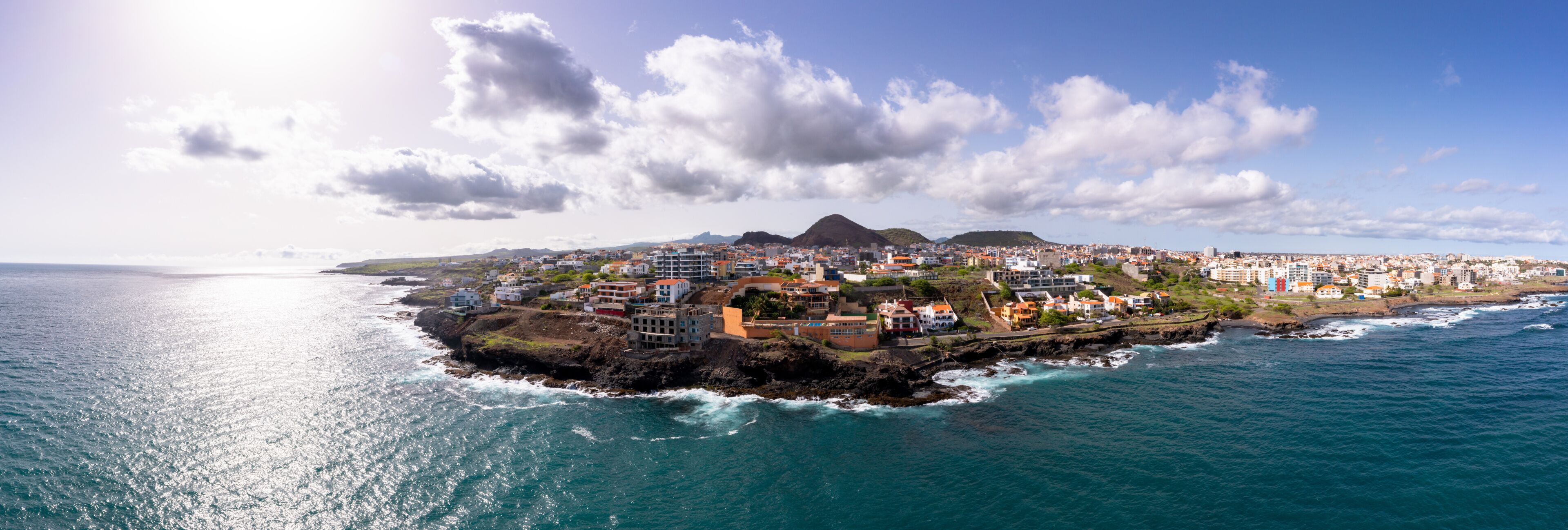 A coastal town with buildings along the shoreline, a prominent hill in the background, and the ocean in the foreground.