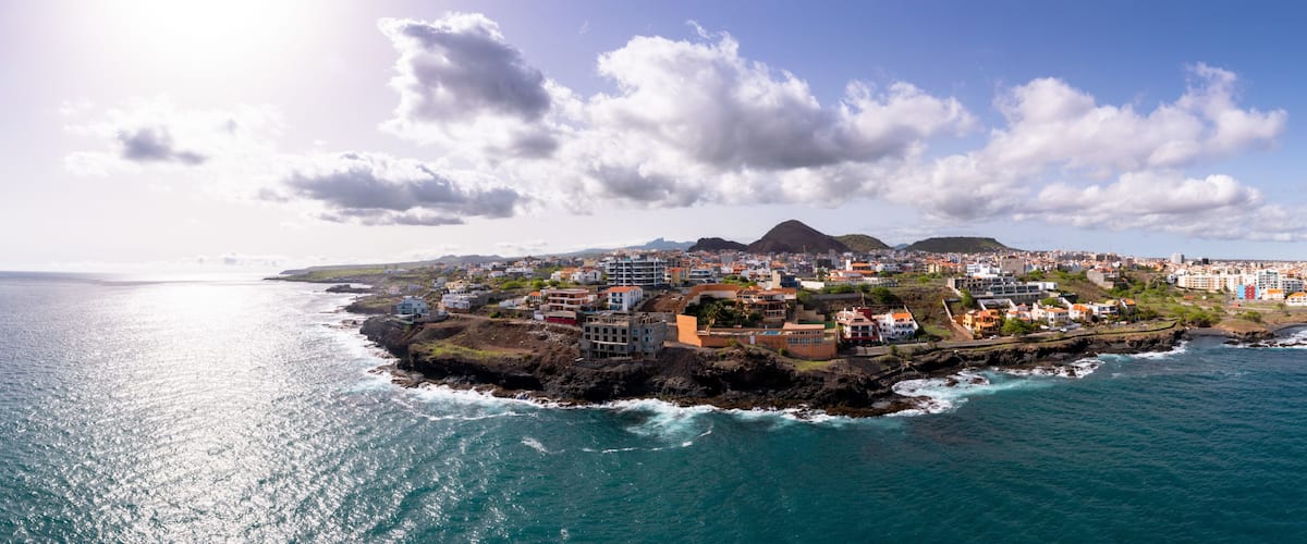 A coastal town with buildings along the shoreline, a prominent hill in the background, and the ocean in the foreground.