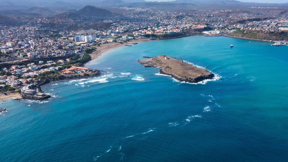 An aerial view of a coastal city with a prominent peninsula, a large body of water, and distant mountains.