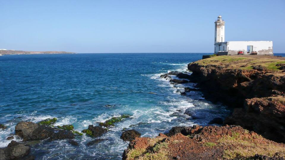 A lighthouse on a rocky coastline with waves crashing against the rocks.