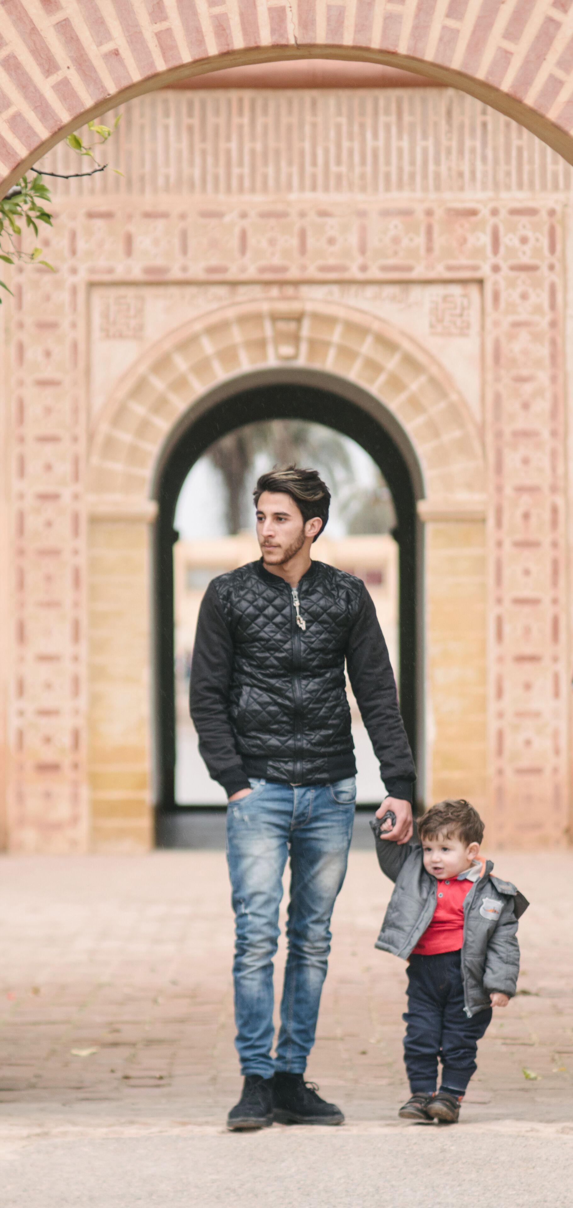 Un hombre y un niño caminando bajo un arco de ladrillo.