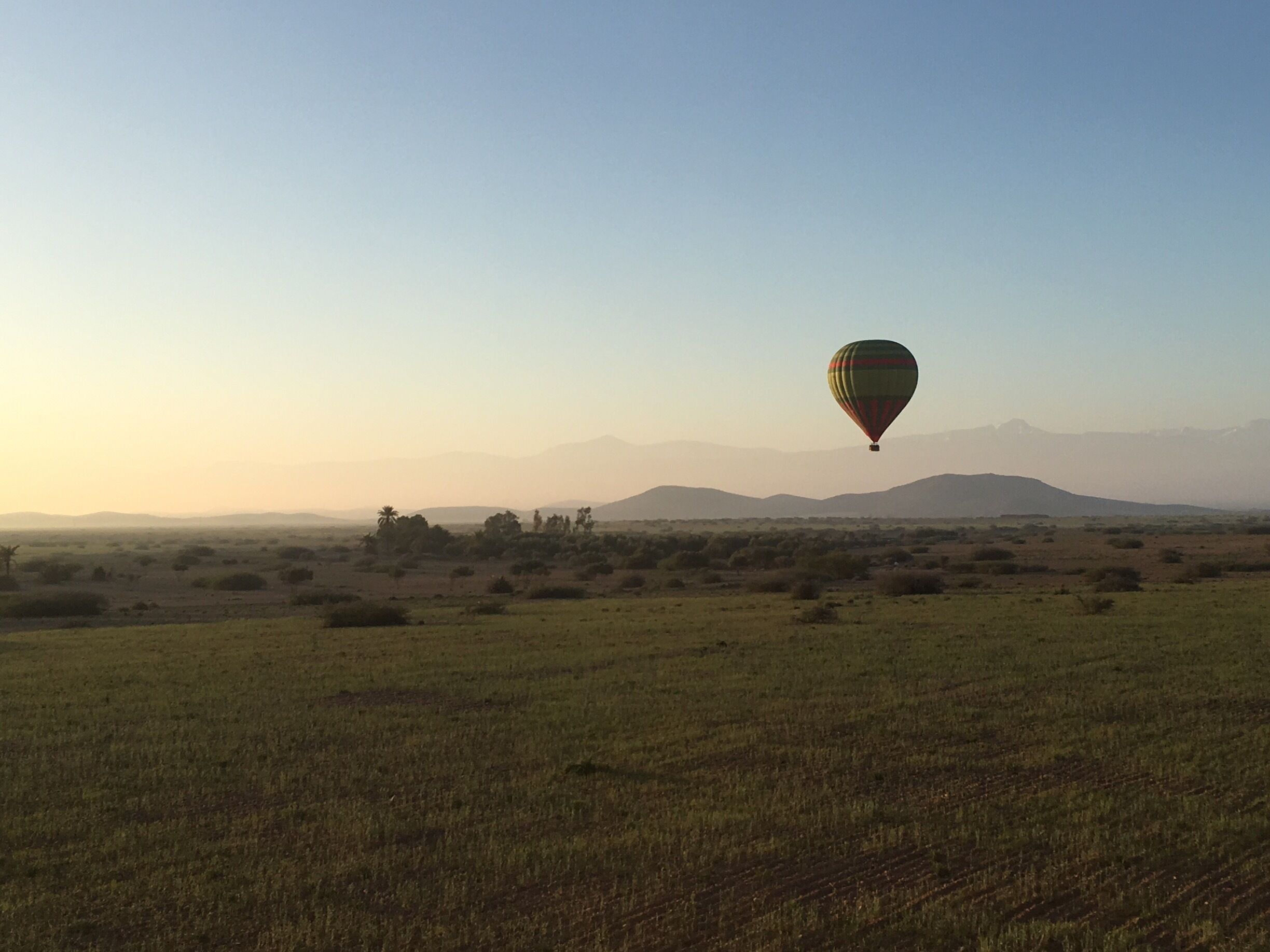 A hot air balloon over a grassy field with distant mountains.