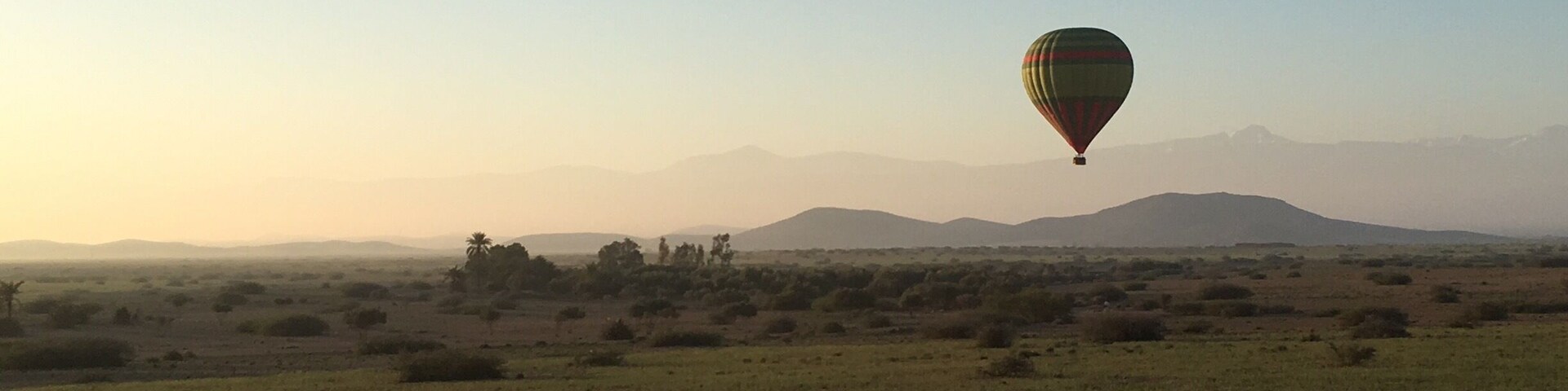 A hot air balloon over a grassy field with distant mountains.
