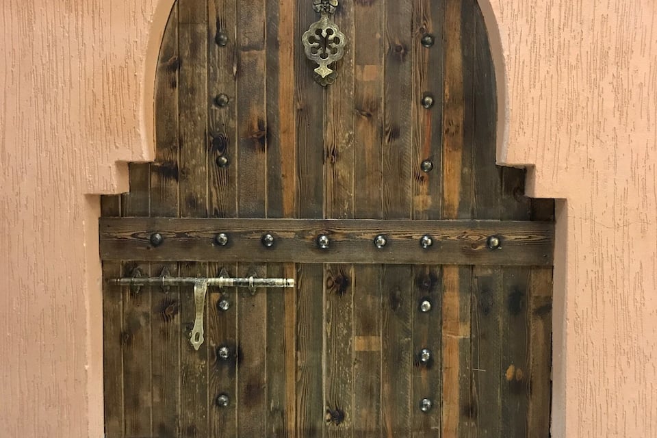 A wooden door with a metal handle and a decorative metal piece above it.