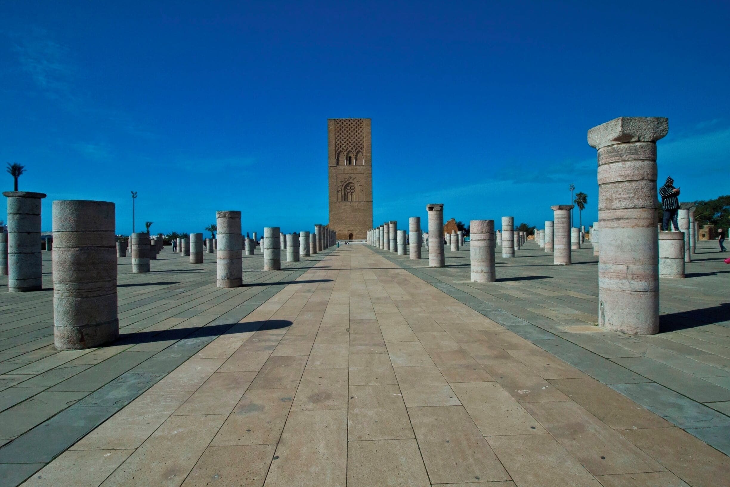 A pathway lined with stone columns leading to a tall tower with intricate carvings.