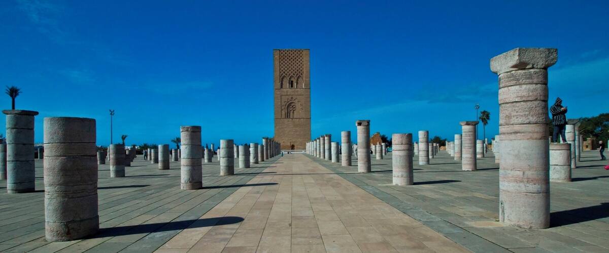 A pathway lined with stone columns leading to a tall tower with intricate carvings.