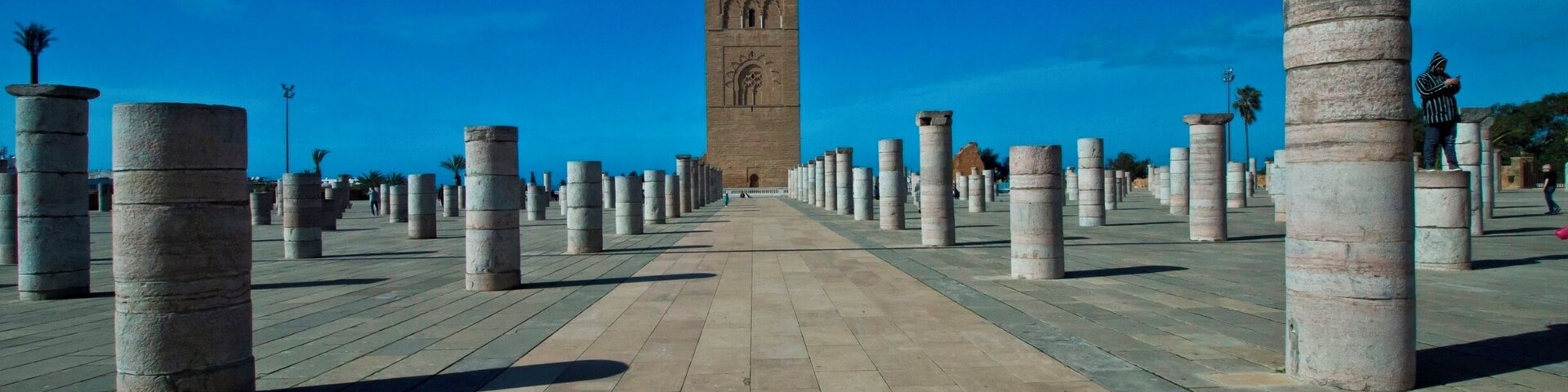 A pathway lined with stone columns leading to a tall tower with intricate carvings.