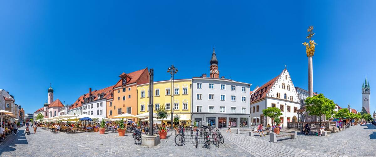 A cobblestone square with colorful buildings, a clock tower, and a statue.