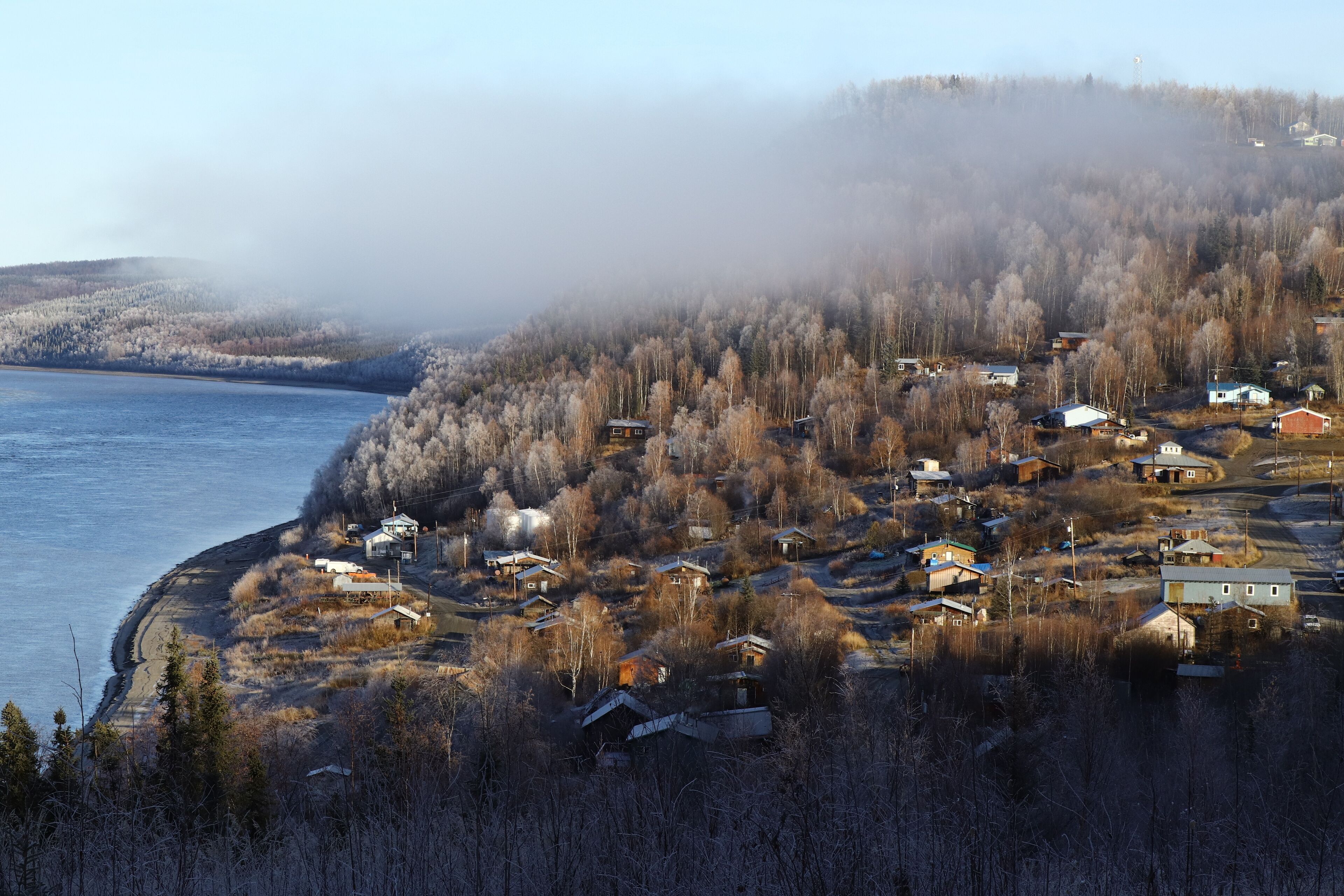A coastal village with houses near a body of water, surrounded by forested hills.