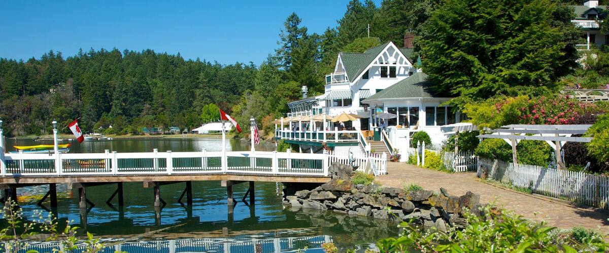 A lakeside lodge with a wooden pier, surrounded by lush greenery and a forested backdrop.