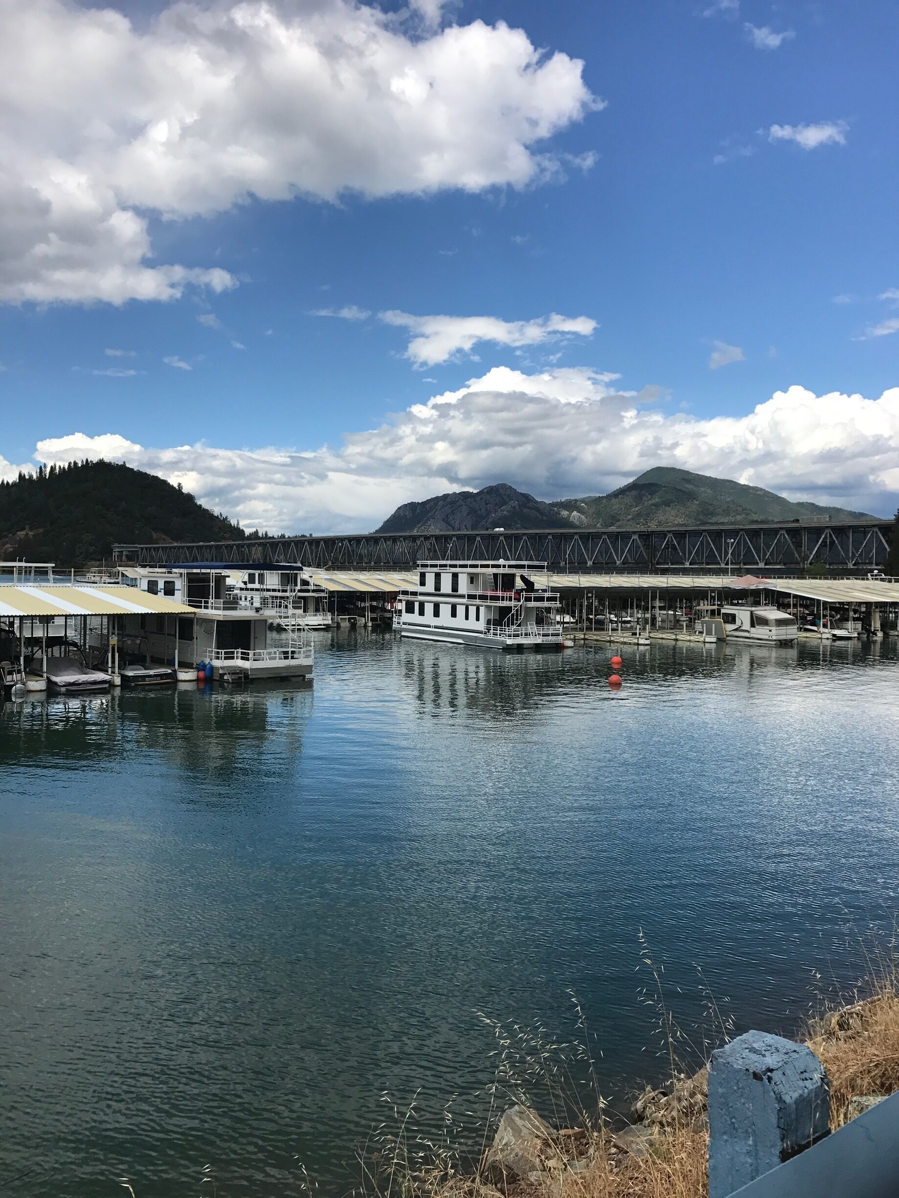 A river with boats docked, a bridge, and mountains in the background.