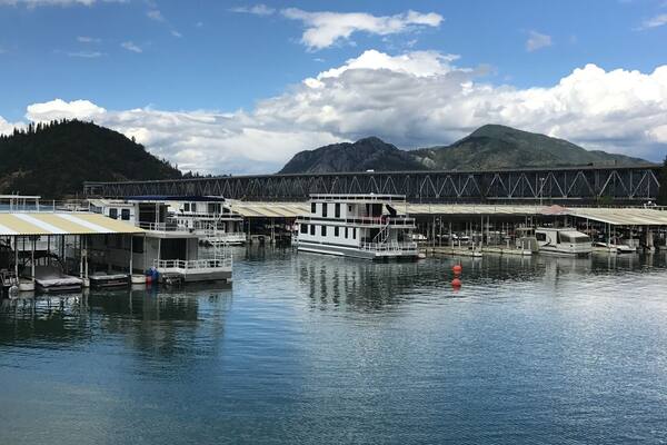 A river with boats docked, a bridge, and mountains in the background.