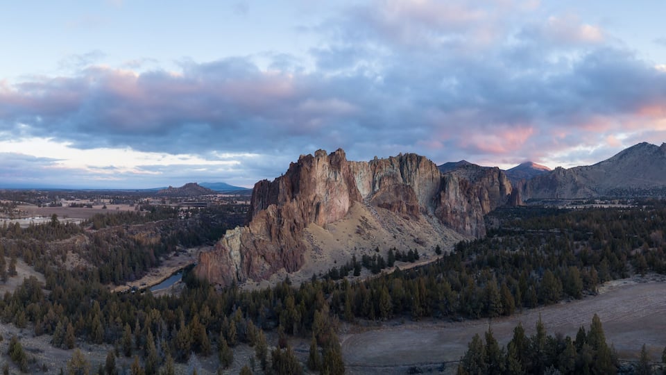 A rugged mountain with a prominent rocky peak, surrounded by dense forests and a valley.