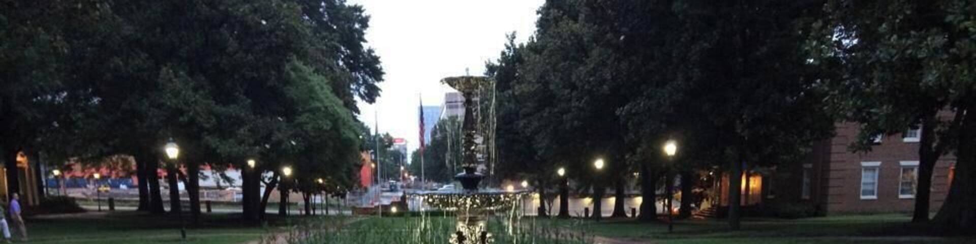 A park with a fountain, a brick plaque, and well-maintained flower beds.