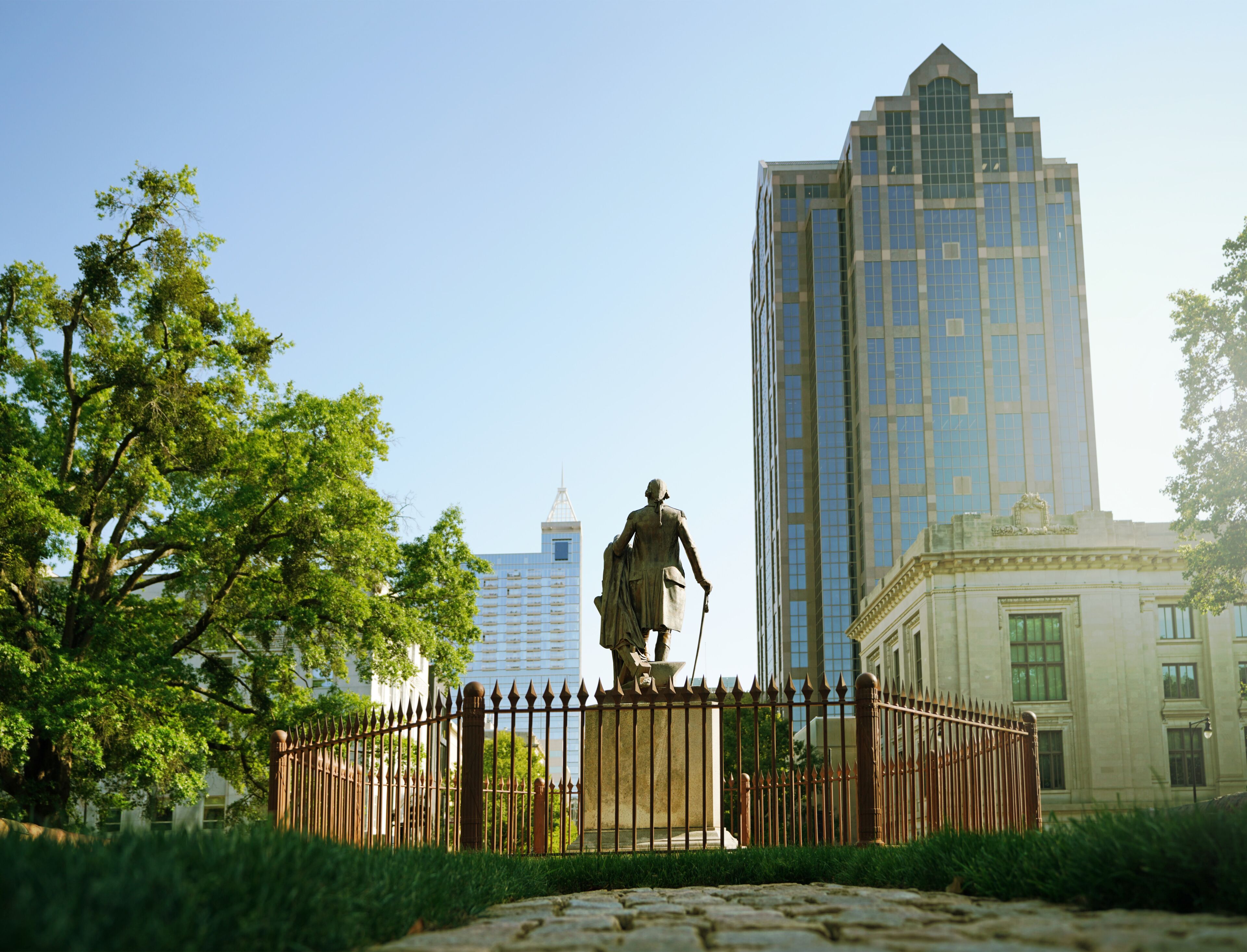 Uma estátua em um parque, com um prédio alto ao fundo.