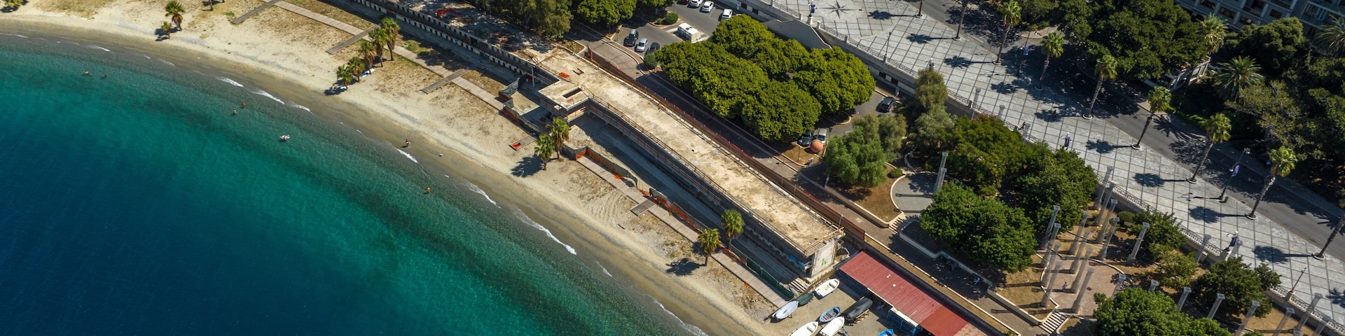 Paisagem costeira com praia, edifícios urbanos e mar azul límpido.