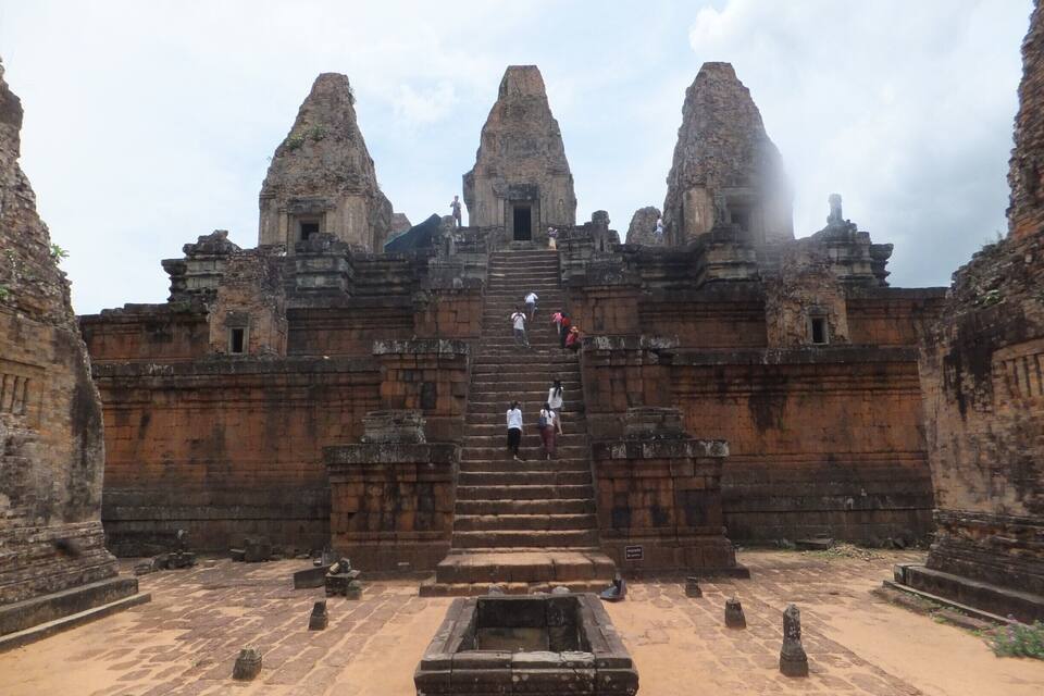 An ancient temple with a central staircase leading to a doorway, surrounded by stone walls and a courtyard.