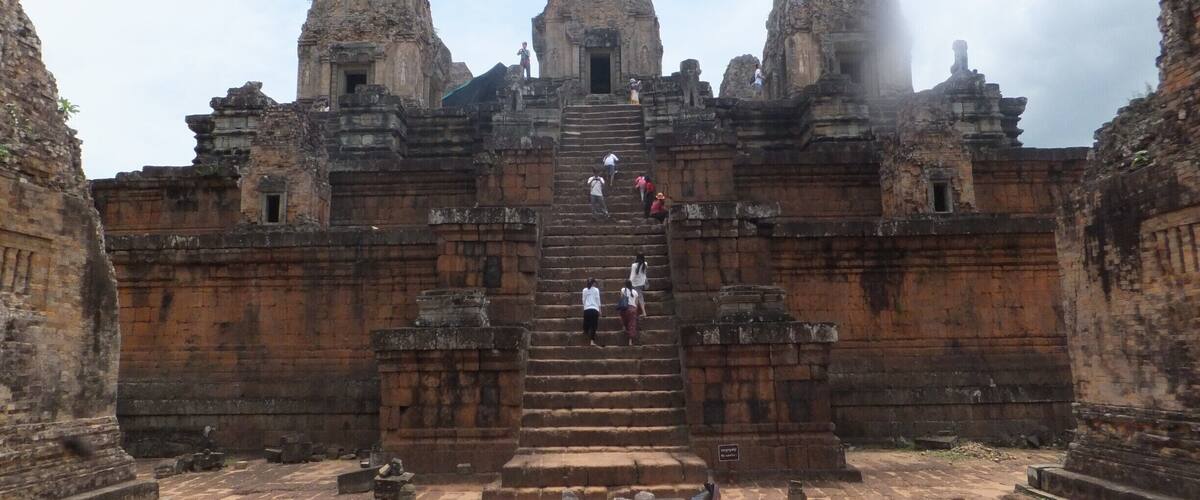 An ancient temple with a central staircase leading to a doorway, surrounded by stone walls and a courtyard.