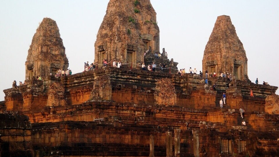 A large ancient temple with three prominent towers and a crowd of people on the upper levels.