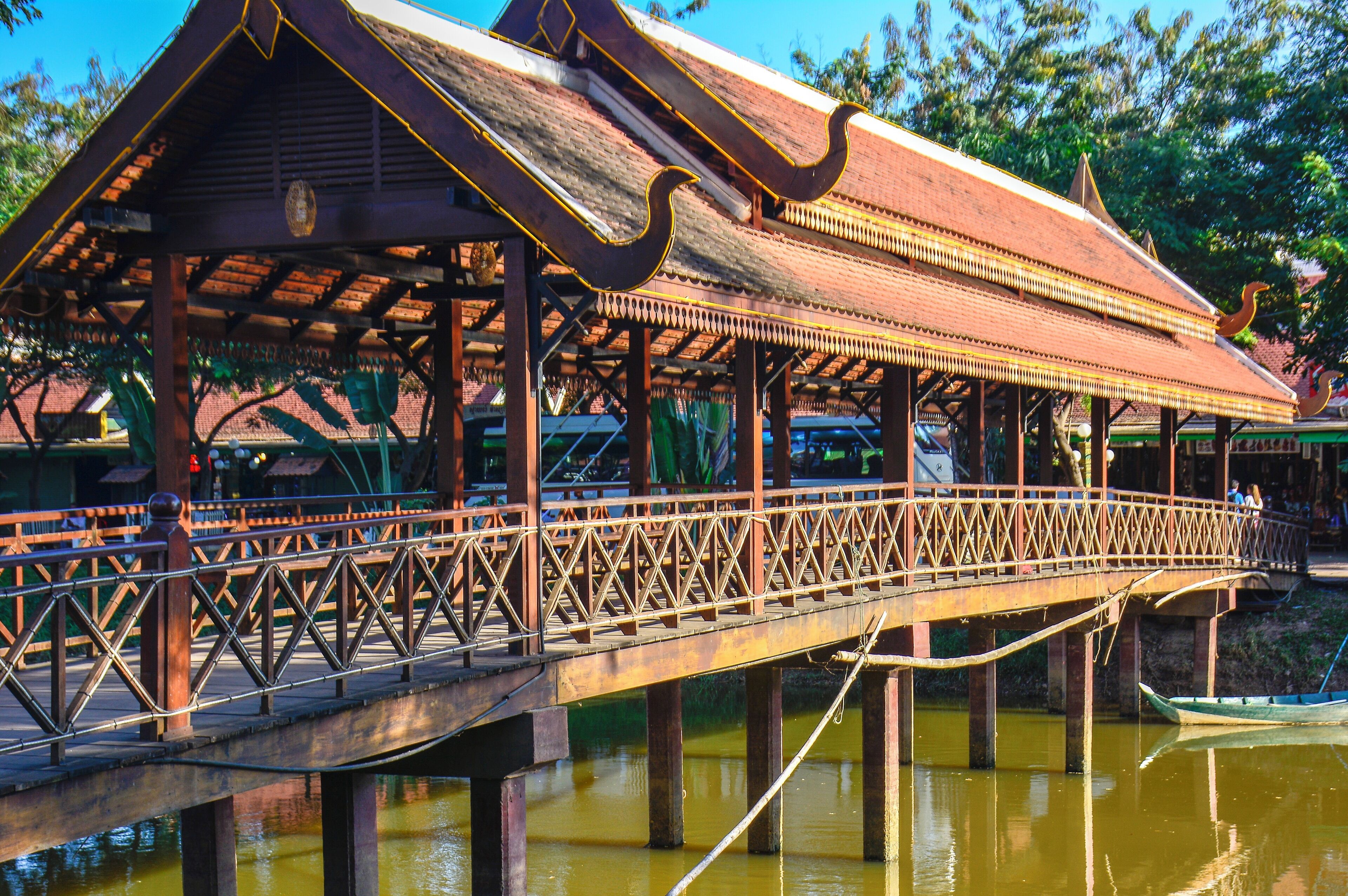 A traditional wooden bridge with a decorative roof, supported by pillars over a body of water.