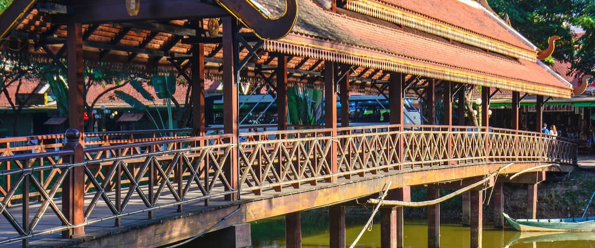 A traditional wooden bridge with a decorative roof, supported by pillars over a body of water.