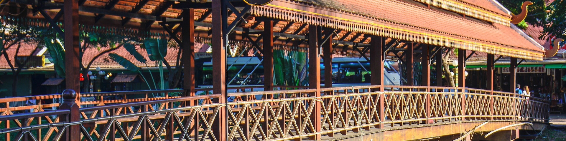 A traditional wooden bridge with a decorative roof, supported by pillars over a body of water.