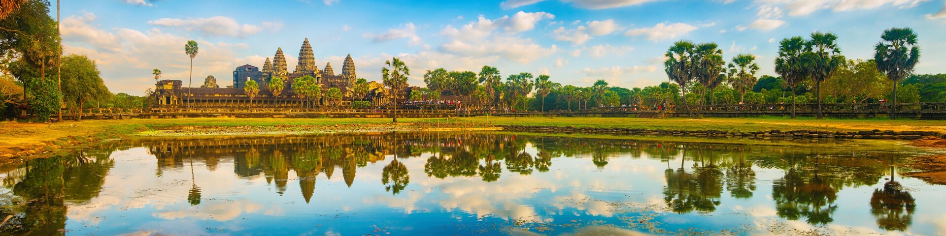 Spiegelbild des Angkor Wat Tempelkomplexes in einem stillen Teich, umgeben von Palmen und einem klaren Himmel.