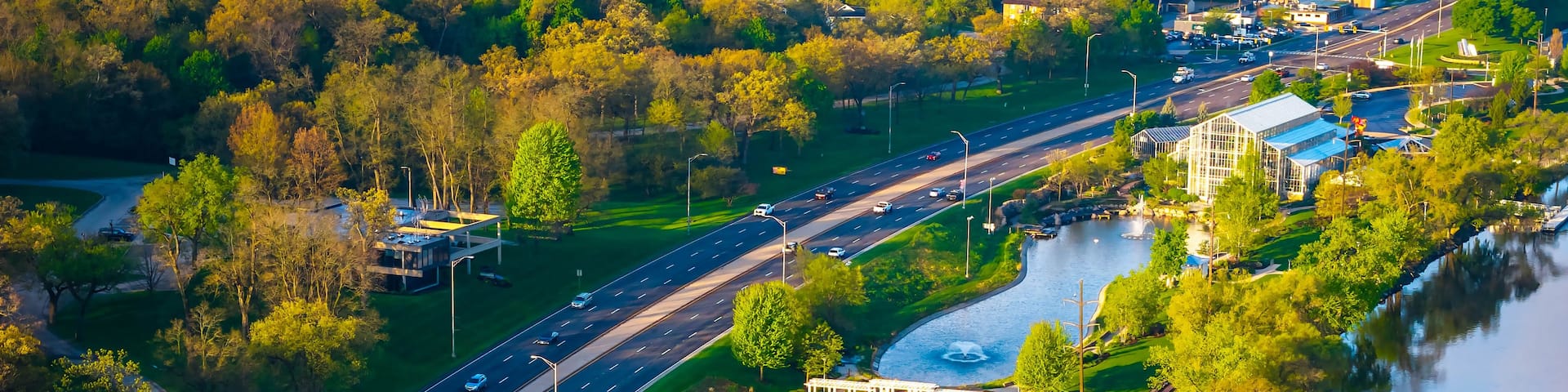 An aerial view of a park with a lake, a road, and a bridge.
