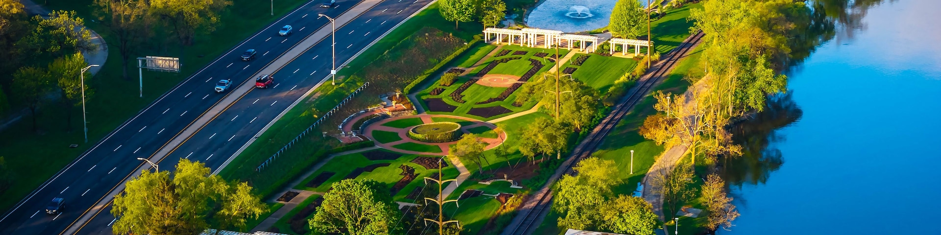 Vista aérea de um parque com um lago, uma estrada e uma ponte.