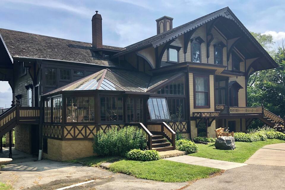 A large, historic house with a prominent bay window, a covered porch, and a staircase leading to the entrance.