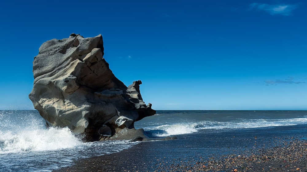 A large rock formation by the ocean with waves crashing against it.