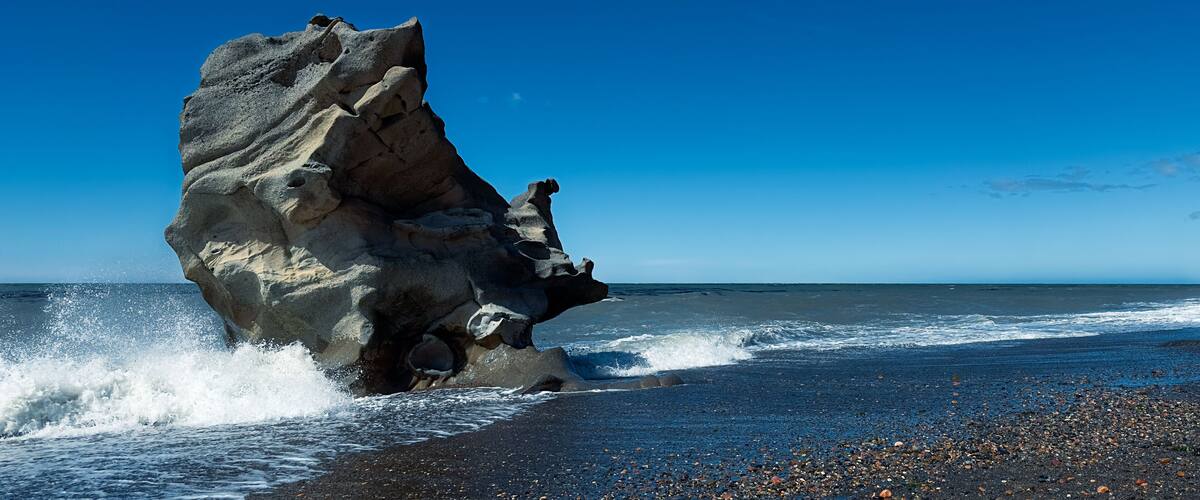 A large rock formation by the ocean with waves crashing against it.